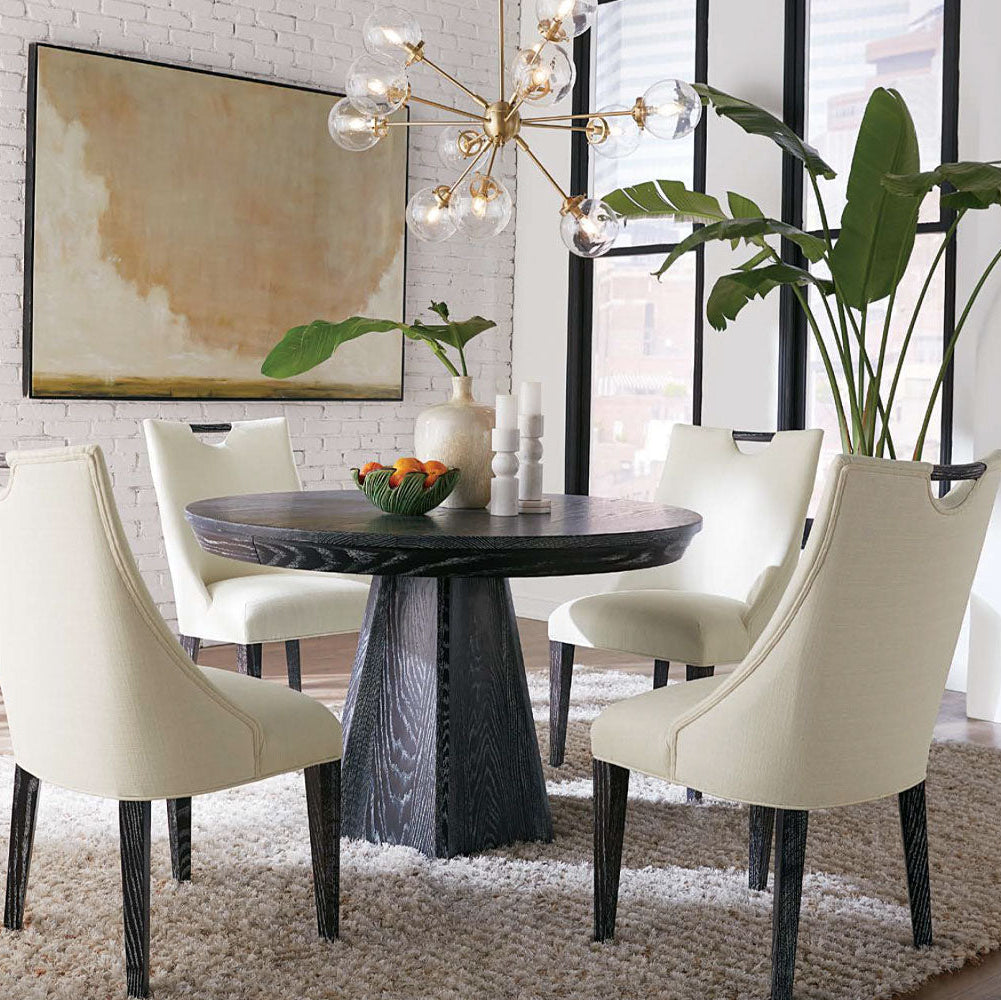 Dining room with a round table and white chairs, featuring a chandelier and artwork on the wall.