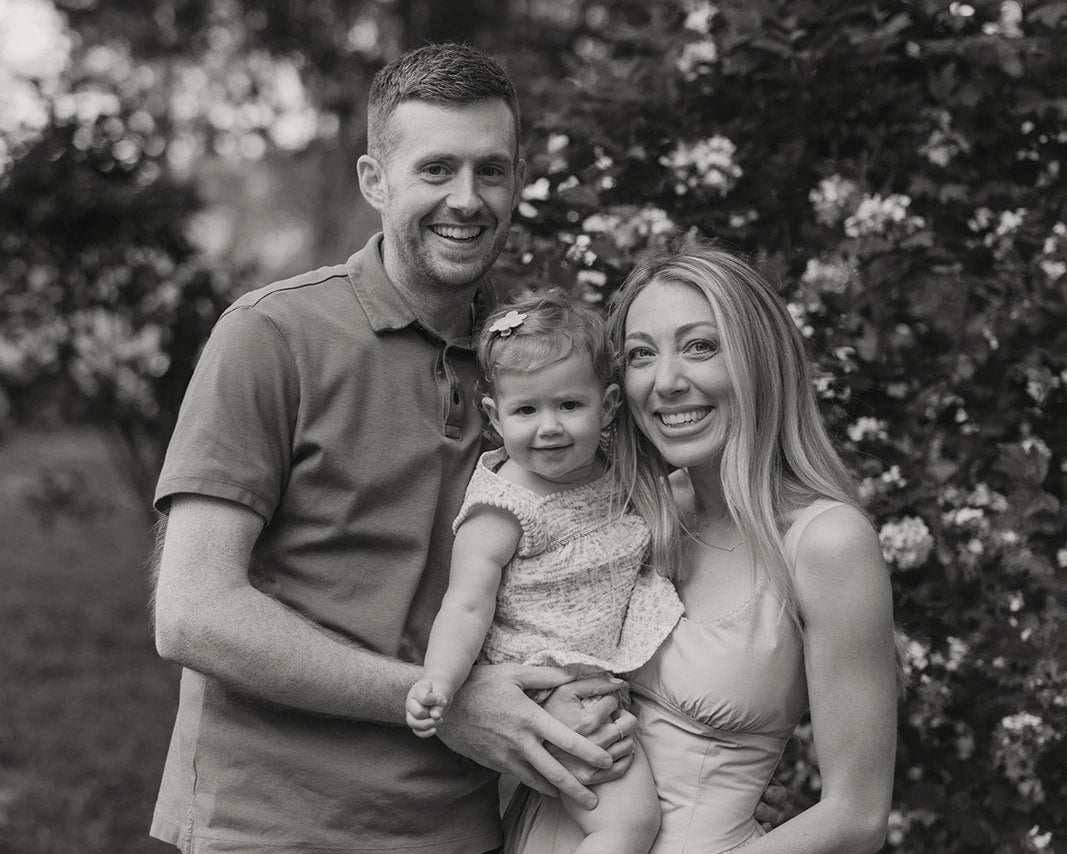 Black and white photo of a family of three standing outdoors with trees in the background